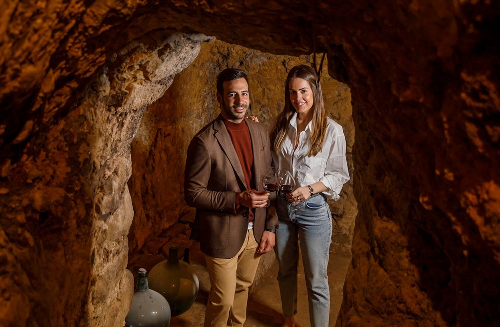 Eduardo Eguren and Carlota holding glasses of red wine in the cellar