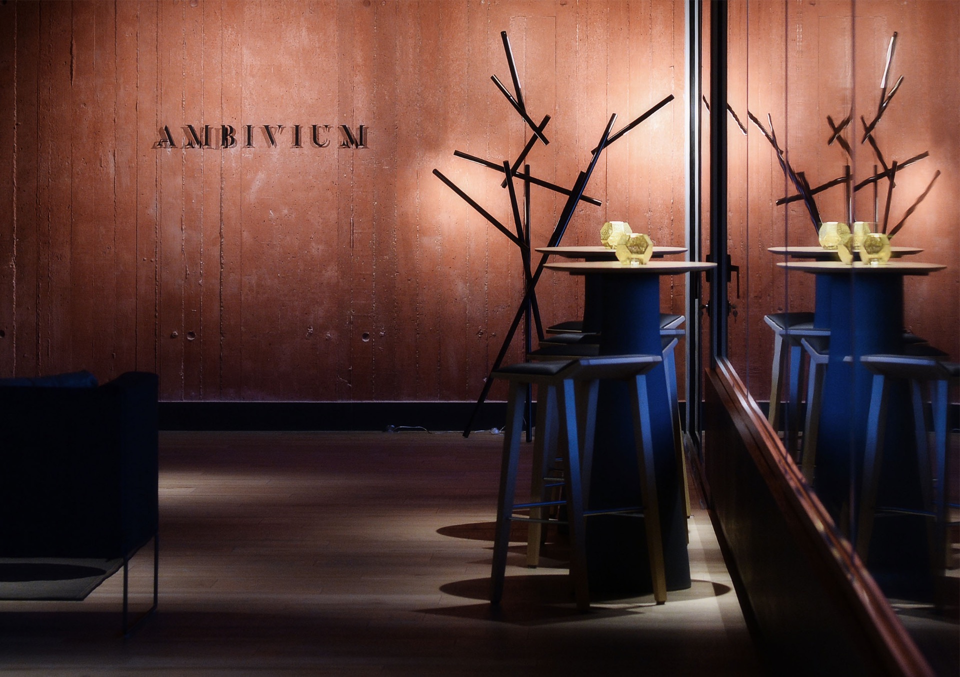 The Ambivium name on a warm concrete wall beside tall tables with golden candle holders
