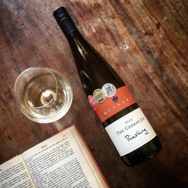 The German Job Riesling beside a glass of white wine and an open book