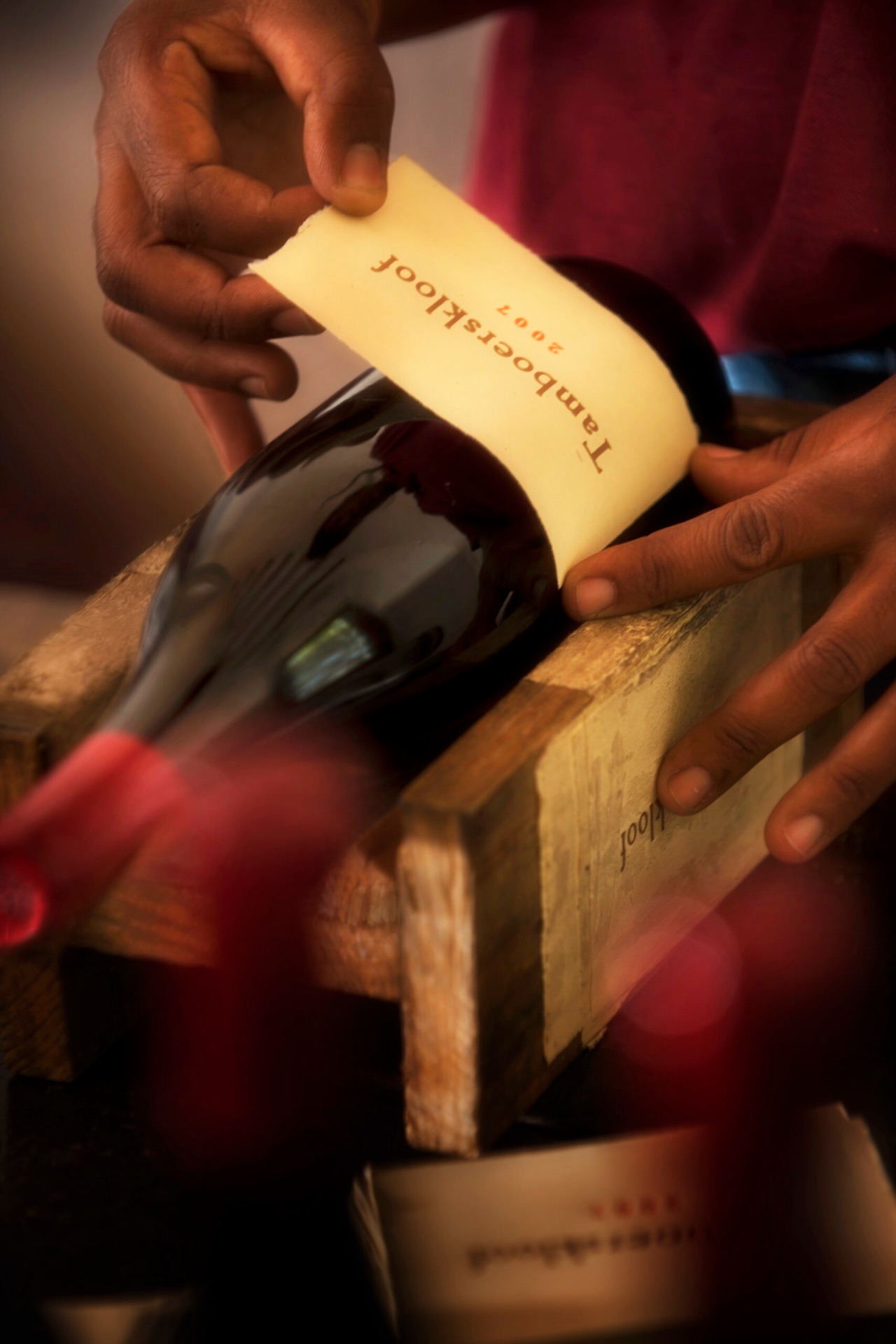 Hands applying a Tamboerskloof paper label to a wine bottle