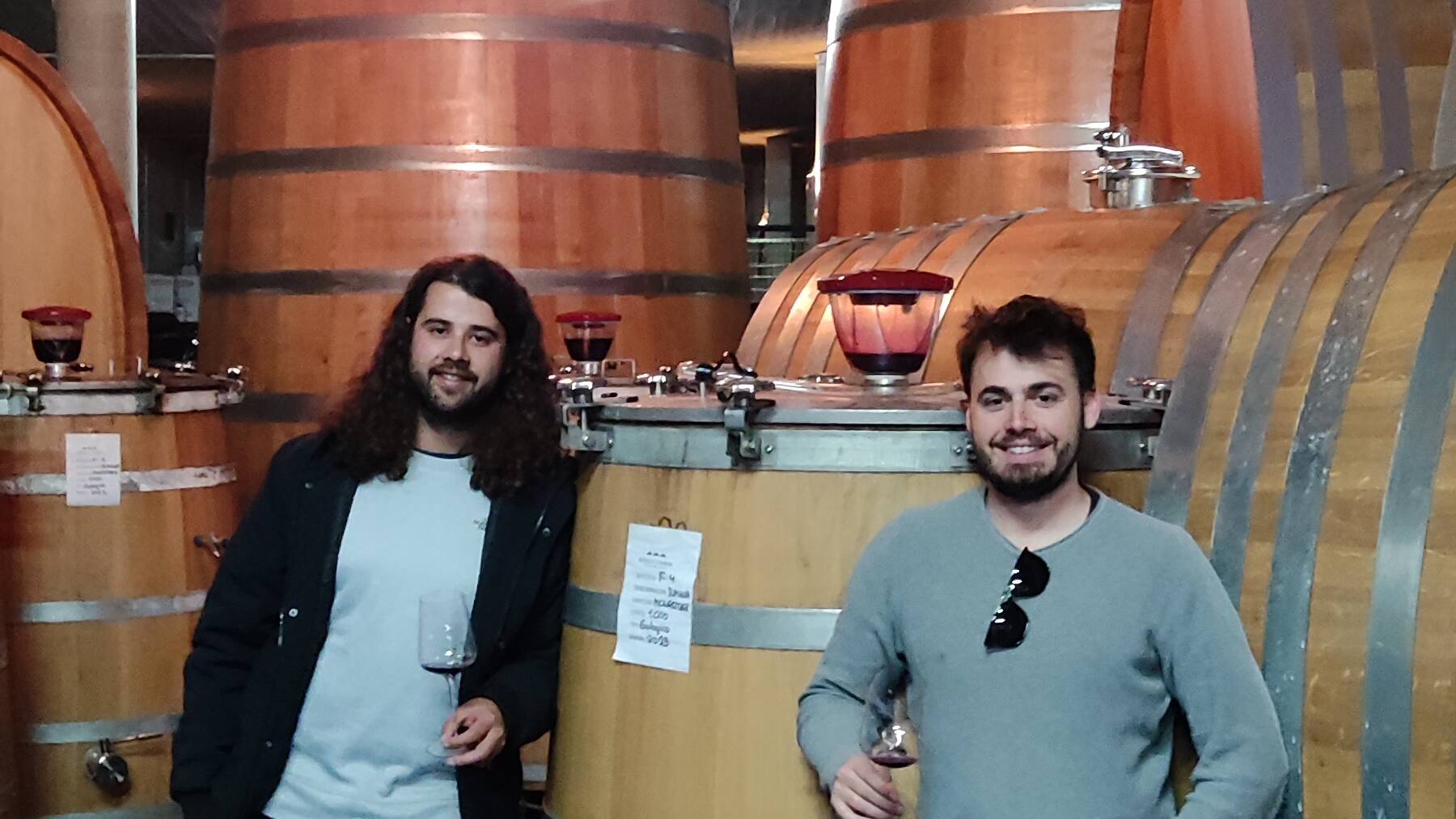 Two winemakers beside large wooden cellar vessels