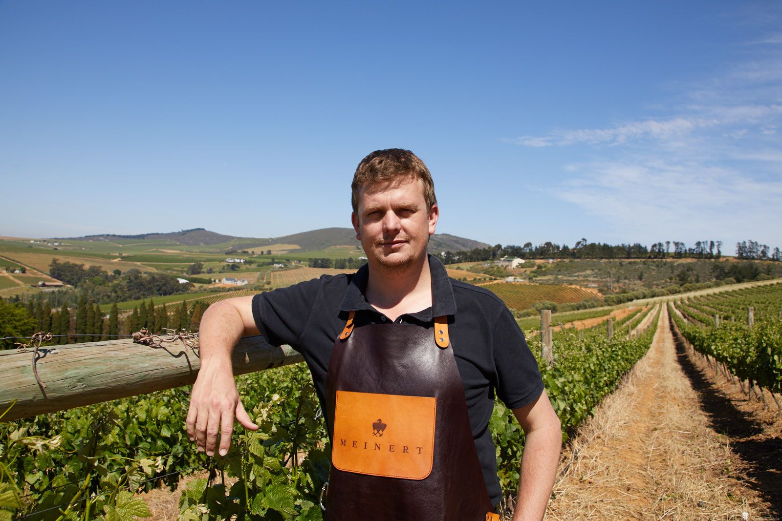 Brendan Butler in a Meinert apron beside a vineyard fence