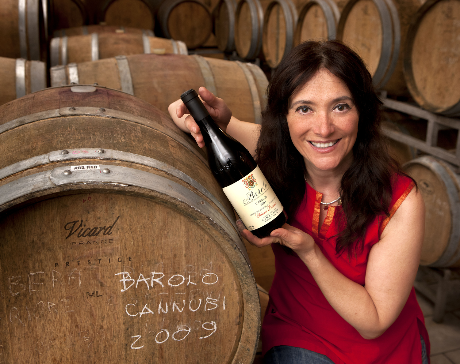 Chiara Boschis beside a barrel holding a bottle of Barolo Cannubi