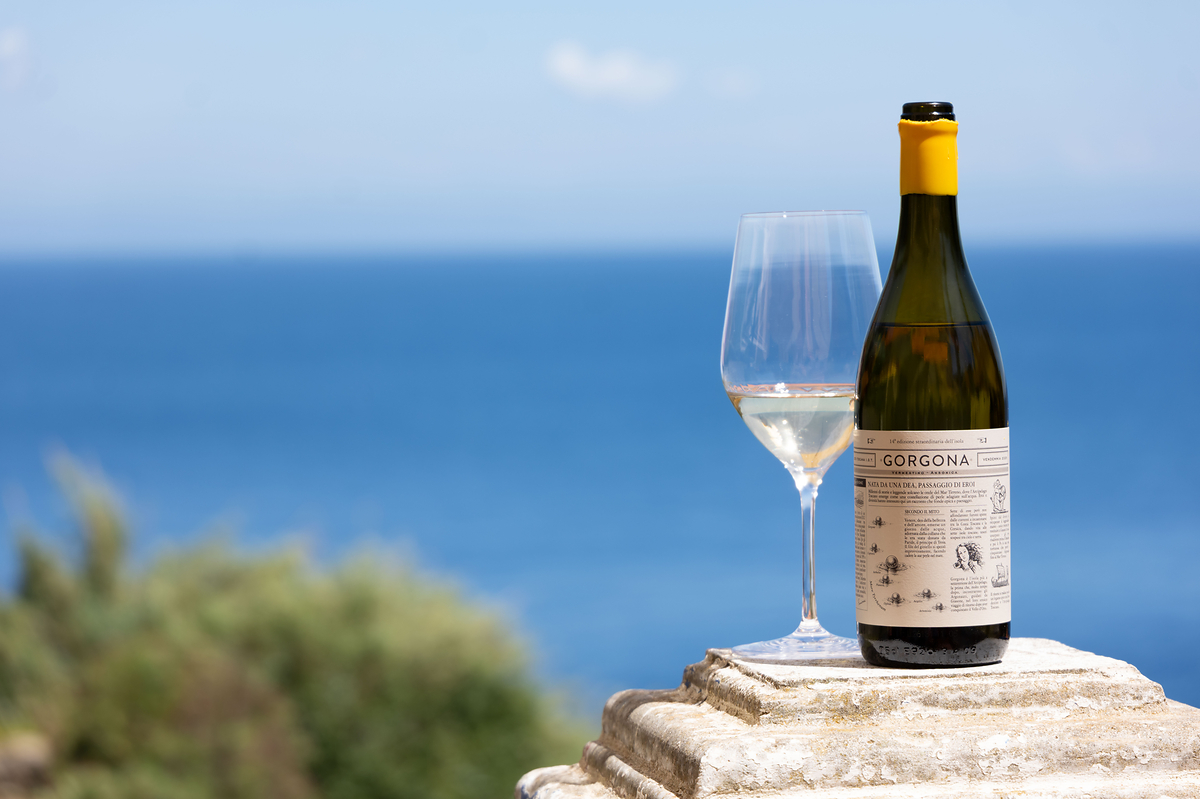 A bottle of Frescobaldi Gorgona and a glass of white wine on a stone pedestal, the sea behind